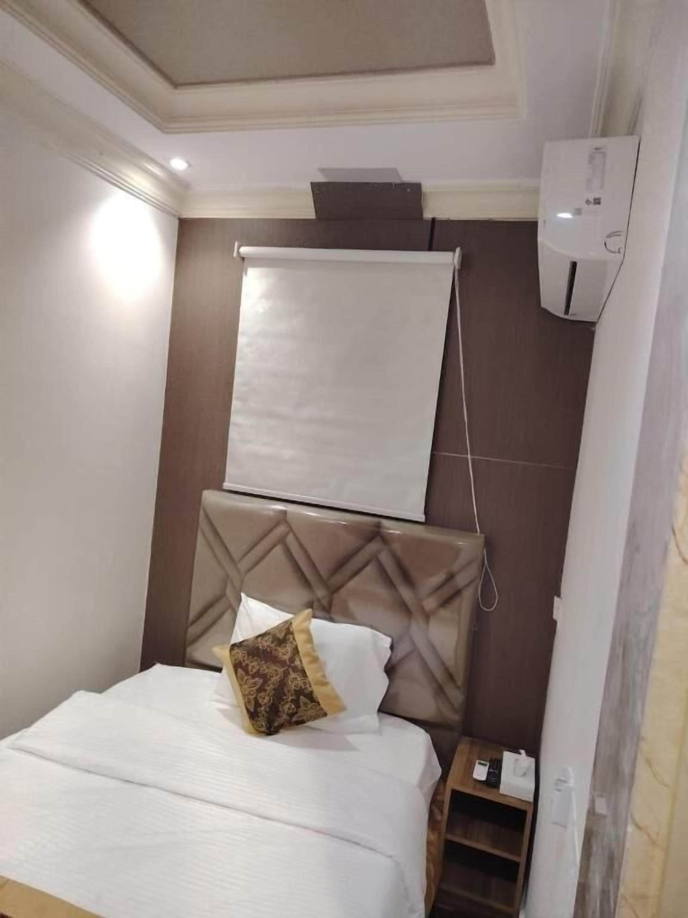 Une chambre d’hôtel avec un lit, une tête de lit, un climatiseur fixé au mur et une fenêtre avec un store blanc.