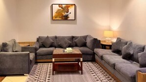 A living room with a grey sofa set, a wooden coffee table, and a patterned rug. - Quiet Rooms 12   (Riyadh)