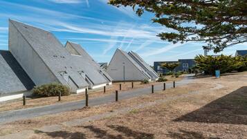 A modern building with a unique sloped roof design, a paved pathway, and a clear sky.