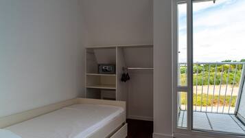 A bedroom with a bed, a white wardrobe, a shelf with a microwave, and a sliding glass door to a balcony.