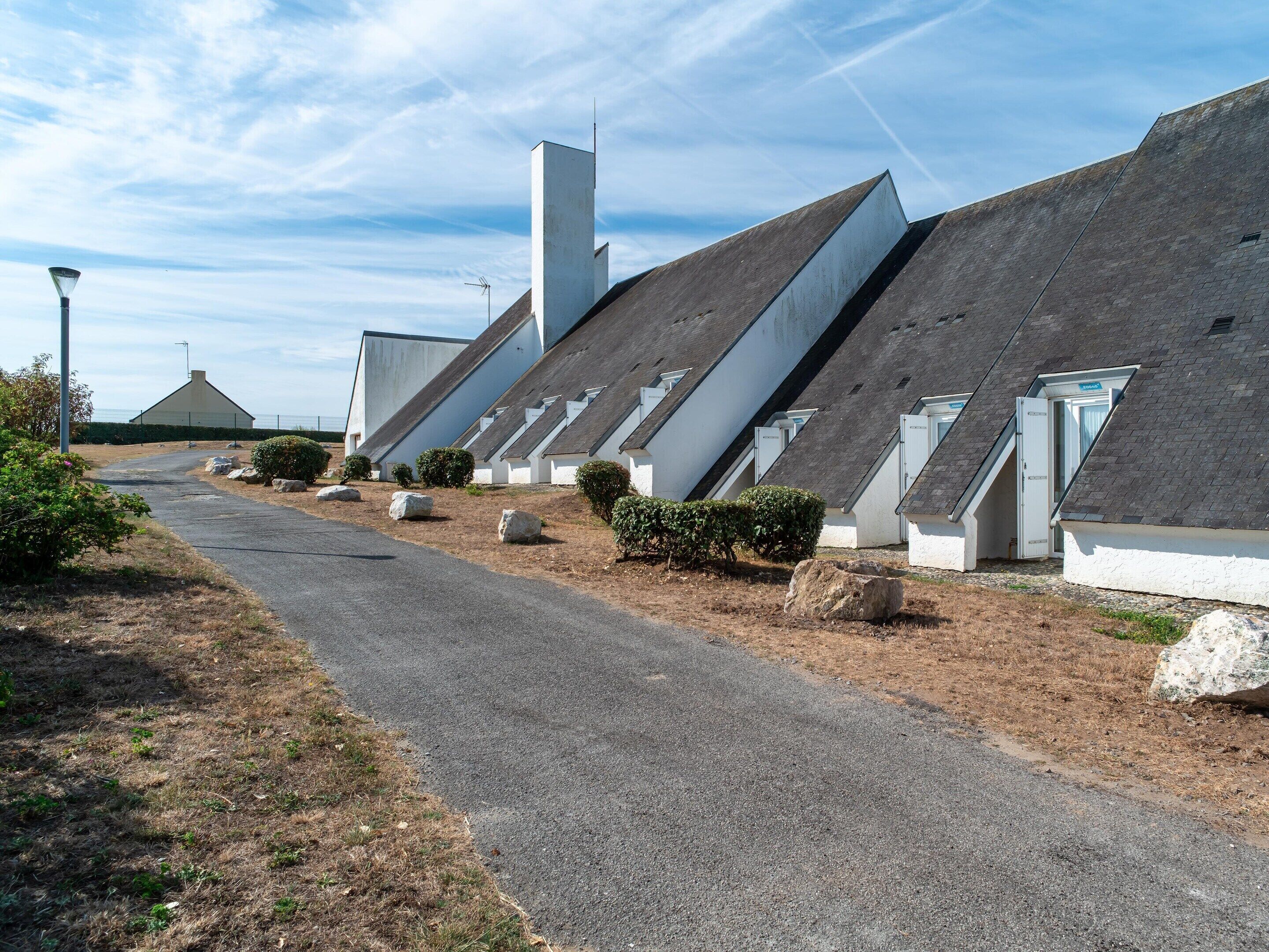 Una hilera de edificios modernos de techos blancos e inclinados, dispuestos a lo largo de un camino pavimentado con vegetación escasa.