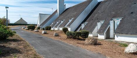 Una hilera de edificios modernos de techos blancos e inclinados, dispuestos a lo largo de un camino pavimentado con vegetación escasa.