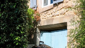 A barbecue grill in a garden with a stone building and blue shutters in the background.