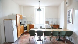 A kitchen with a dining table, chairs, a refrigerator, cabinets, a stove, and a hanging light fixture.
