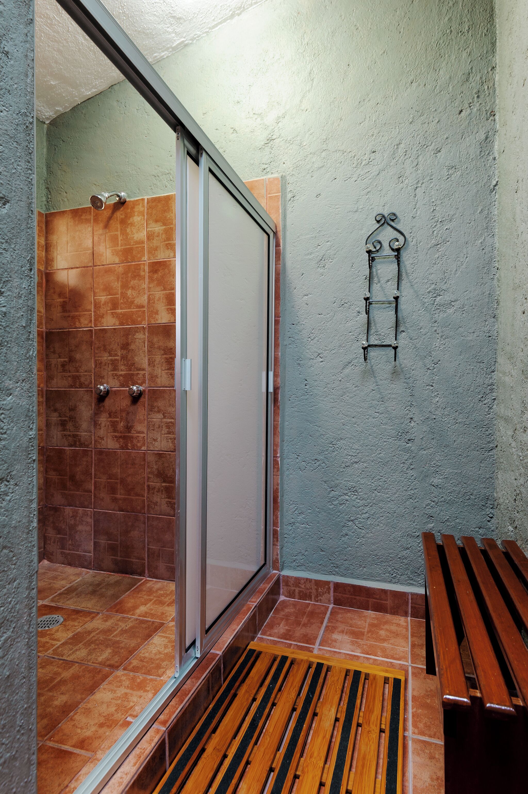 Een badkamer met een douche, een bankje en een handdoekhouder.