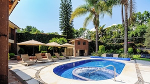 A circular pool with a hot tub, lounge chairs, and umbrellas. - Casa Avándaro (Valle de Bravo)