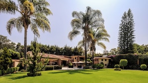 A well-maintained garden with palm trees, a patio area, and a building with a tiled roof. - Casa Avándaro (Valle de Bravo)