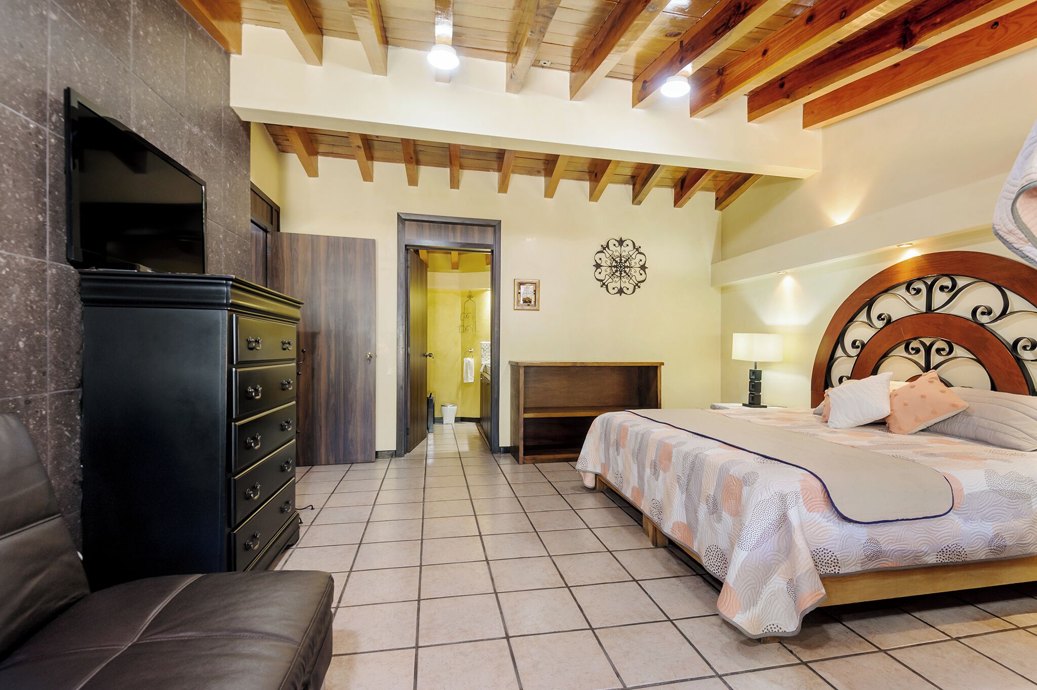A bedroom with a bed, dresser, and a television mounted on the wall.