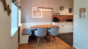 Una cocina moderna con comedor, armarios de madera, una cafetera y una lámpara colgante.