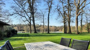 Una mesa de madera con sillas en un parque con un lago y árboles al fondo.