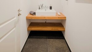 Un baño estrecho con un lavamanos blanco, encimera de madera y un espejo redondo con luz.