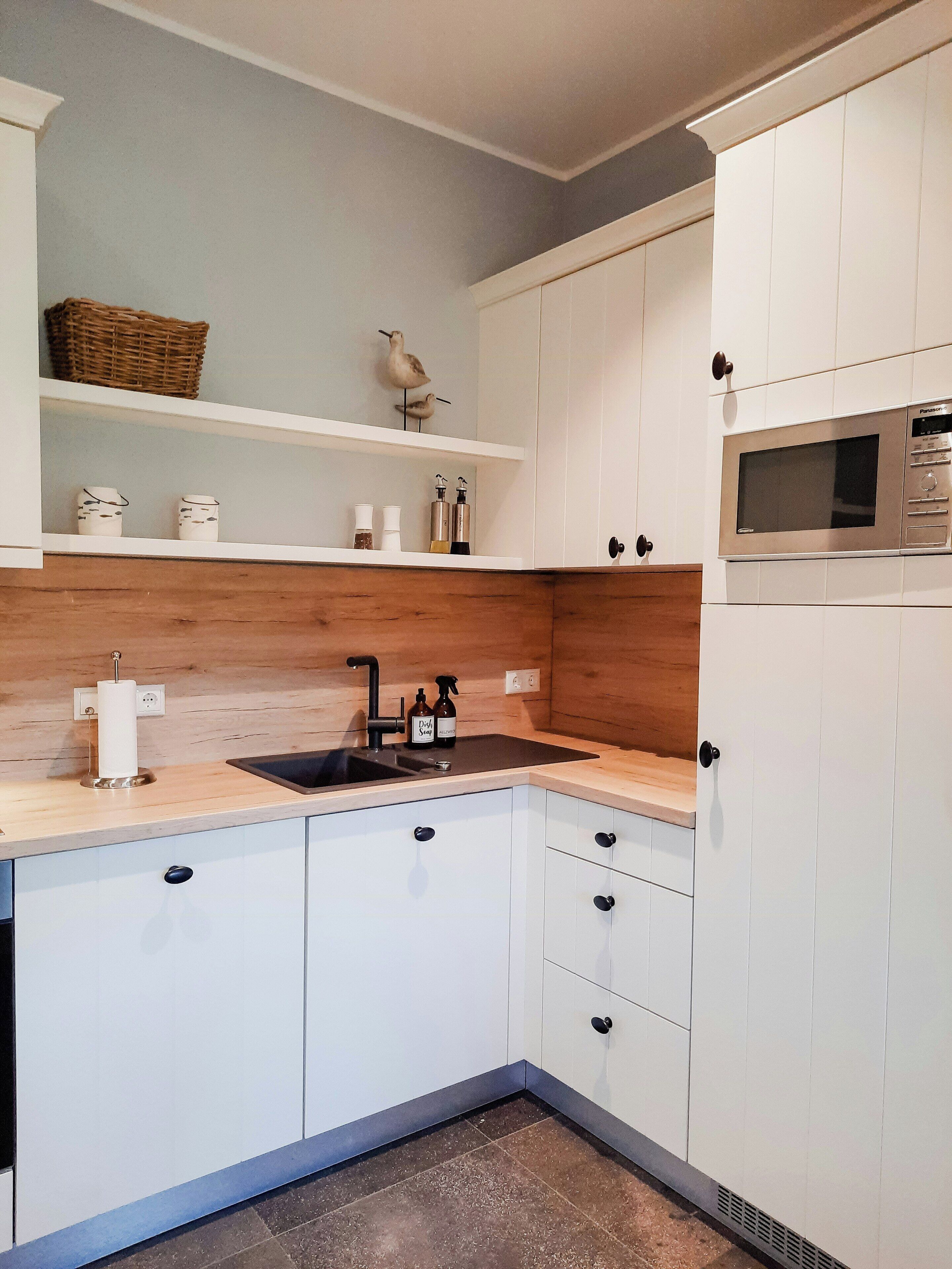Een moderne keuken met witte kasten, een houten aanrechtblad, een ingebouwde magnetron en een spoelbak.