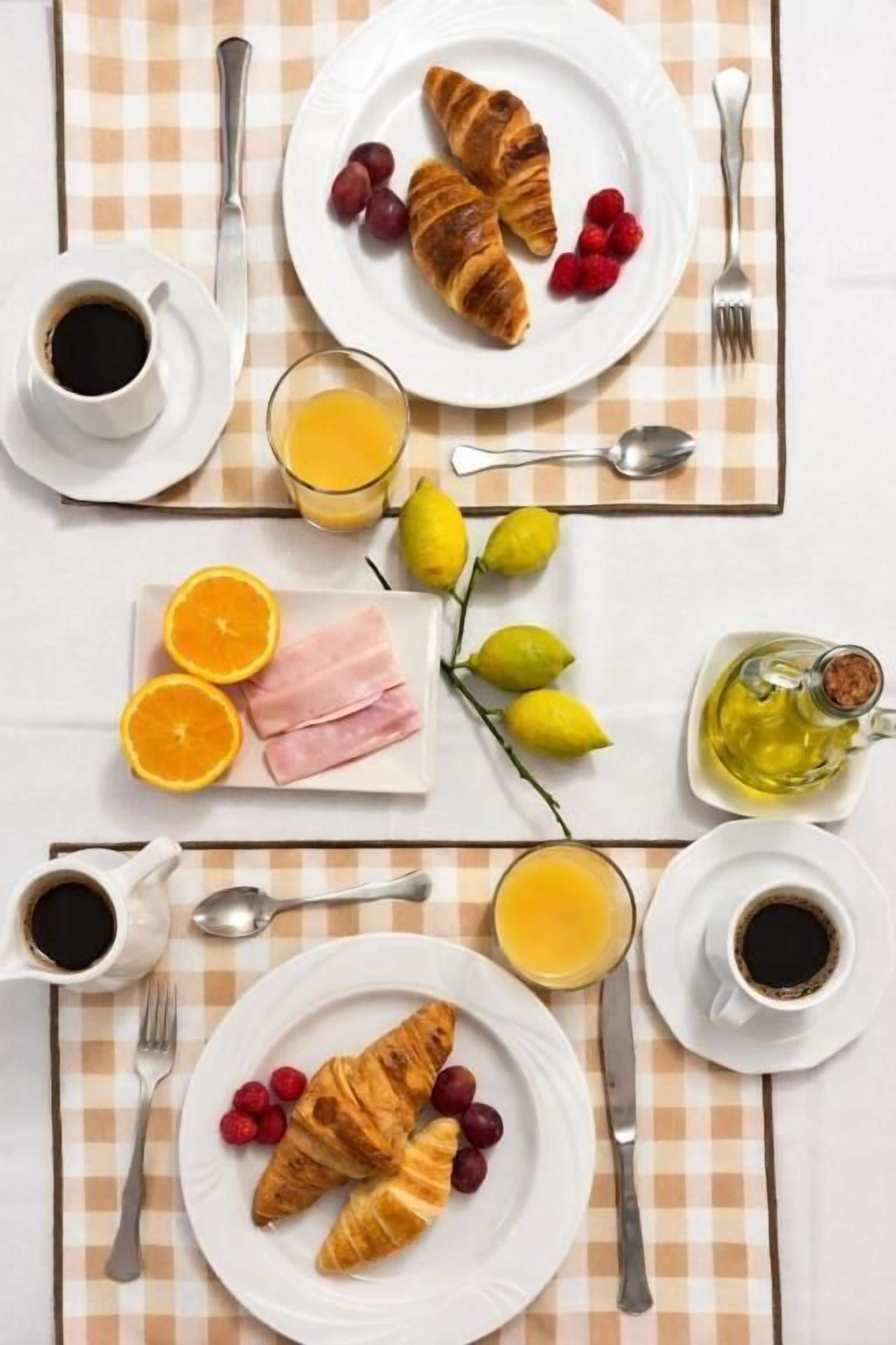 A breakfast setup with croissants, grapes, orange slices, and juice on a checkered tablecloth.