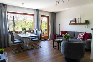 Uma sala de estar moderna com área de jantar, janelas amplas e um sofá cinzento.