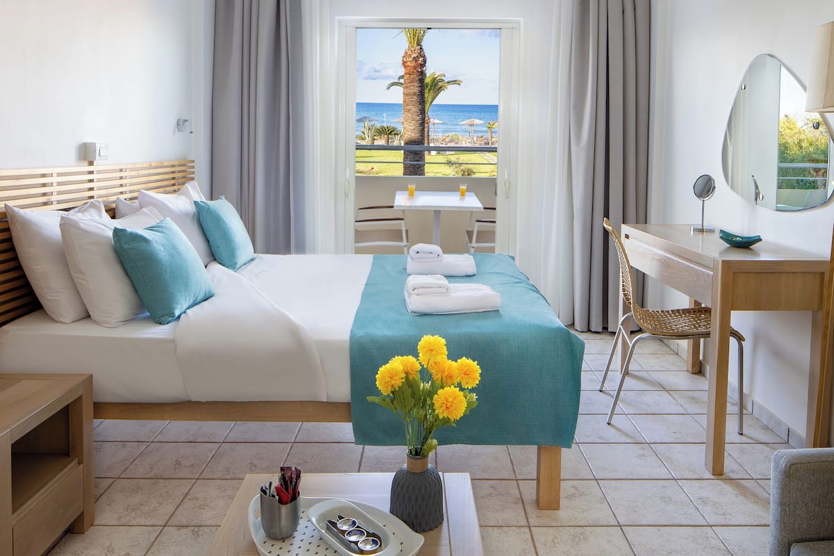 A hotel room with a bed, a desk, a chair, a small table, and a view of the ocean.