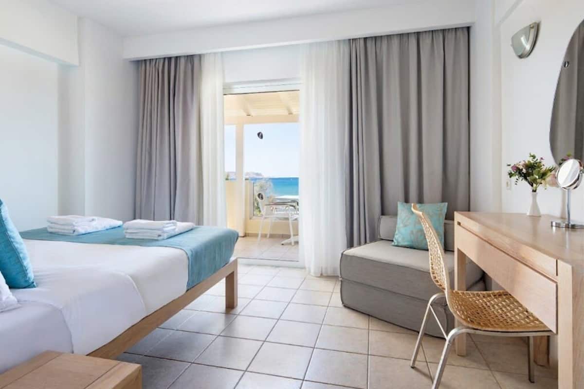 A hotel room with a bed, a desk, a chair, and a view of the sea.