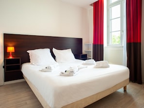 A neatly made bed with white linens and towels, a bedside table with a lamp, and a window with curtains. - Retreat, Heated Pool & 2 Beds (Dinan)
