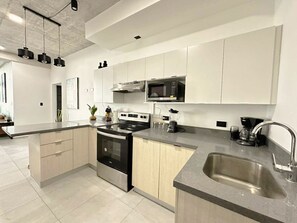 Una cocina moderna con armarios blancos, un lavamanos de acero inoxidable, un horno empotrado y un microondas.