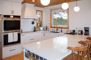Une cuisine moderne avec des meubles blancs, un four double, un grand îlot central et des chaises en bois.