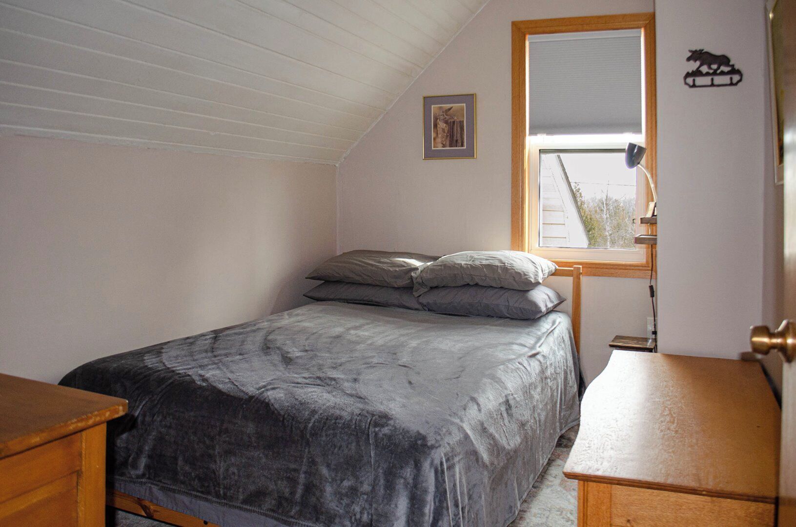 Et soveværelse med seng, natbord, kommode, et vindue og en vægmonteret lampe.