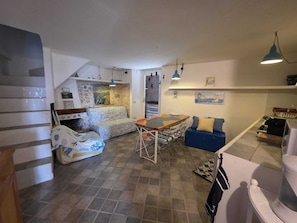 A compact living space with a dining area, a sofa, a small kitchen, and a staircase.