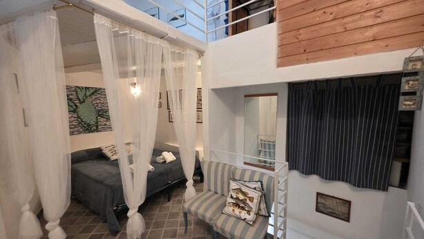 A bedroom with a canopy bed, a striped chair, a mirror, and a view of the sky through a skylight. - La Casa Bianca nel Borgo - by Be Your Home (San Felice Circeo)