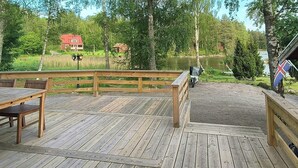 A wooden deck with a table and chairs, overlooking a lake and surrounded by trees.