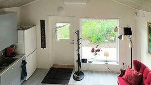 A compact kitchen with a sink, a refrigerator, and a coffee maker. There is a door leading to a garden with a window and a lamp.