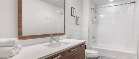 Un baño moderno con lavamanos, tocador y bañera blancos.