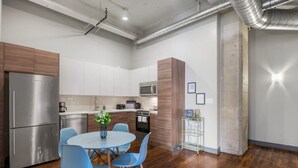 Une cuisine moderne dotée d’appareils électroménagers en acier inoxydable, un coin repas avec des chaises bleues et un plancher en bois.