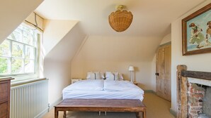 Ein Schlafzimmer mit Bett, einer Holzbank, einem Heizkörper, einem Fenster, einer Wandleuchte und einem Kamin.