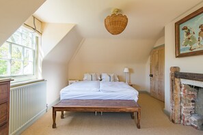 Ein Schlafzimmer mit Bett, einer Holzbank, einem Heizkörper, einem Fenster, einer Wandleuchte und einem Kamin.