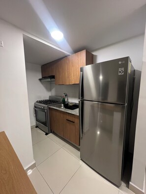A compact kitchen with a stainless steel refrigerator, a gas stove, wooden cabinets, and a tiled floor. - Deluxe Apartment with City Views At Worldwide (Panamá)
