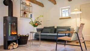 A living room with a wood-burning stove, a sofa, a wicker chair, a table with a vase of flowers, and a lamp. - Oasis of peace near the lake (Langen Jarchow)