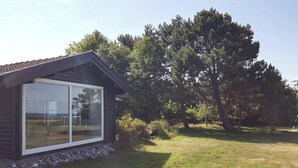 Ett modernt hus med stora glasfönster, en fasad av tegel och en gräsklädd trädgård med träd.