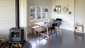Ett rum med en vedeldad kamin, ett matbord med stolar och ett litet skåp.