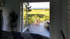 A room with a bed, a cactus, and a view of a deck with potted plants and a bench. - Wake up with water views from Omø (Omø)