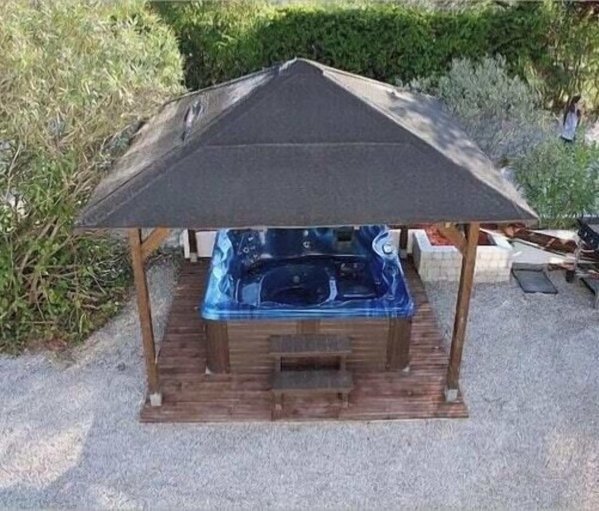 A wooden gazebo with a sloped roof, a hot tub, and a gravel base.