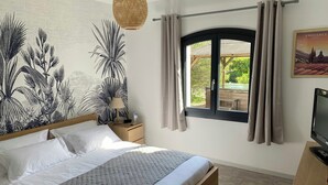 Ein Schlafzimmer mit Bett, Nachttisch, Lampe, Fernseher, Fenster mit Vorhängen und einer Wand mit einem botanischen Wandbild.