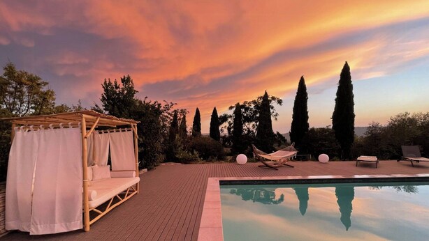 Ein Poolbereich mit Holzterrasse, Baldachinbett und freiem Blick zum Himmel.