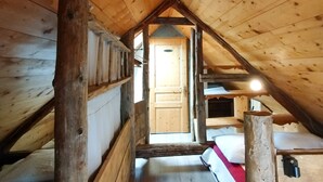 Een houten kamer op zolder met stapelbedden, een houten deur en een schuine balklaag.