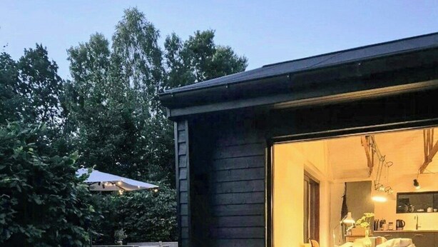 Uma casa moderna com terraço, área de refeições e uma grande porta de vidro que dá para o interior.