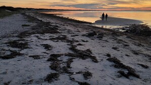 Uma praia com costa rochosa, mar calmo e céu ao pôr do sol.