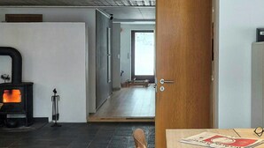 Quarto com teto de madeira, chão de pedra, uma mesa com cadeiras, uma porta e uma lareira.