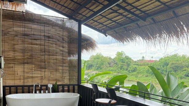 A modern bathroom with a freestanding bathtub, a wooden floor, and a view of lush greenery.