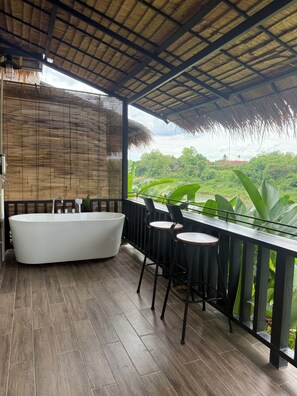Ein modernes Badezimmer mit freistehender Badewanne, Holzboden und Blick auf üppiges Grün.