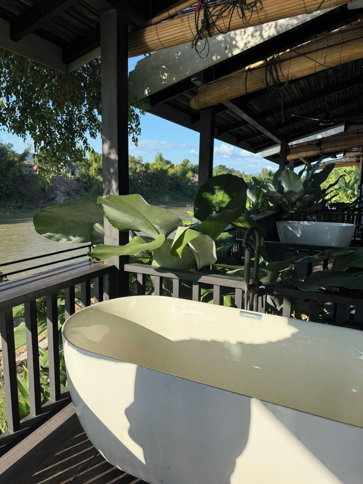 Un baño con una bañera grande, una terraza de madera y vistas a un río.