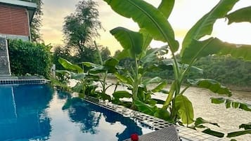 A poolside setting with a dining setup on a boat, surrounded by lush greenery and a view of a river.