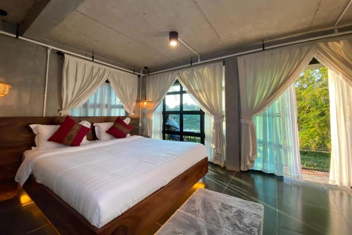 Un dormitorio con una cama grande, cortinas y vistas por la ventana.