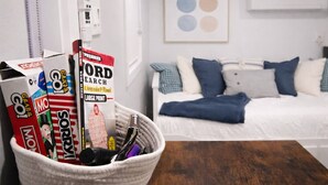 A neatly organized room with a bed, pillows, a framed artwork, and a basket with books and pens.
